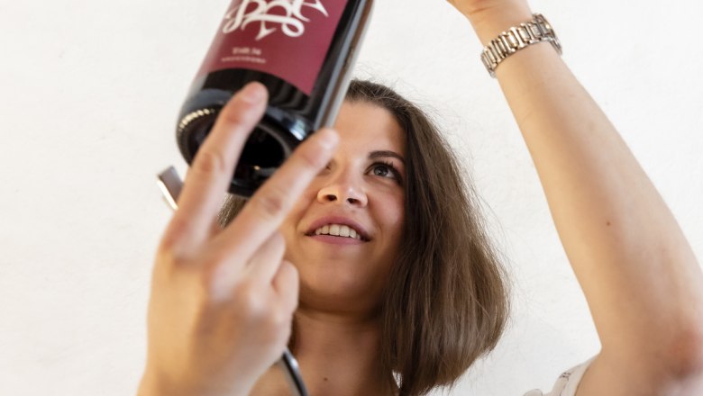 Neue Weinlinie, © Rainer Friedl Frau inspiziert eine Weinflasche gegen das Licht.