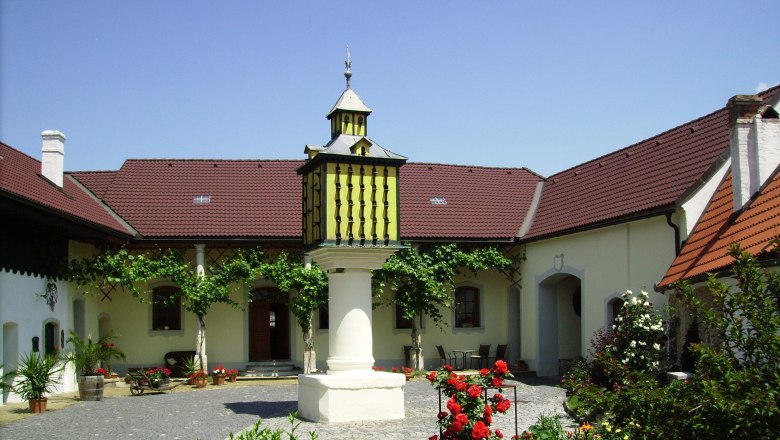 Innenhof, © Andreas Fischer Ein gepflegter Innenhof mit Blumen, einem zentralen Brunnen und einem Gebäude mit roten Dächern.