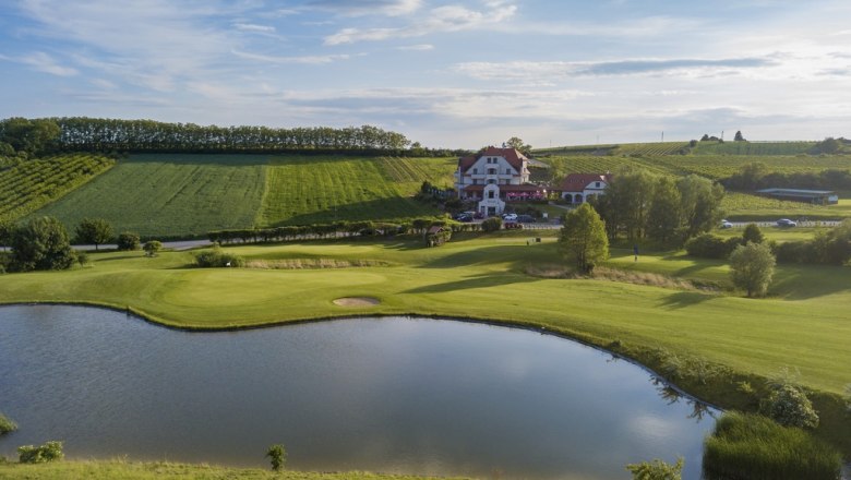 Golfclub Poysdorf, © Golfclub Poysdorf Landschaftsaufnahme eines Golfplatzes mit Teich und Clubhaus im Hintergrund.