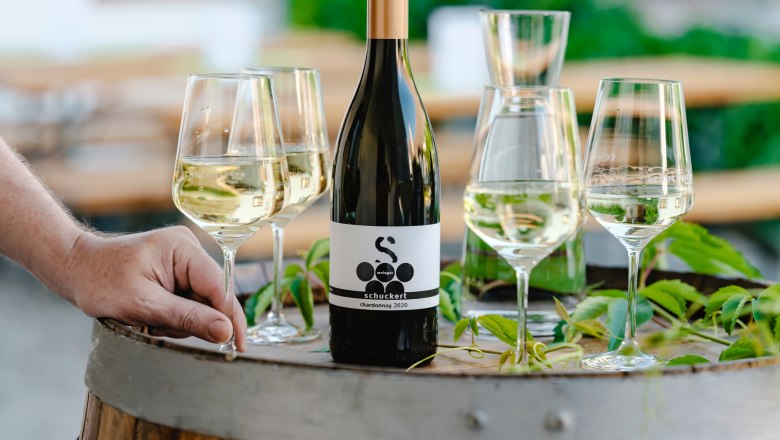 Weingut Schuckert, © Michael Reidinger Weinflasche und Gläser auf einem Weinfass im Freien.