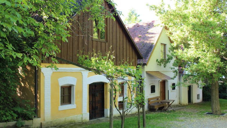 Kellergasse Wolkersdorf, © Weinviertel Tourismus Traditionelle Weinkeller in der Kellergasse von Wolkersdorf, umgeben von grünen Bäumen und Weinreben.