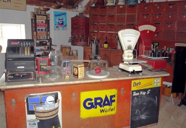 Museum für Dorfkultur in Grossengersdorf, © Museum für Dorfkultur in Grossengersdorf Innenansicht eines historischen Dorfladens mit Waage, Registrierkasse und alten Werbeschildern.