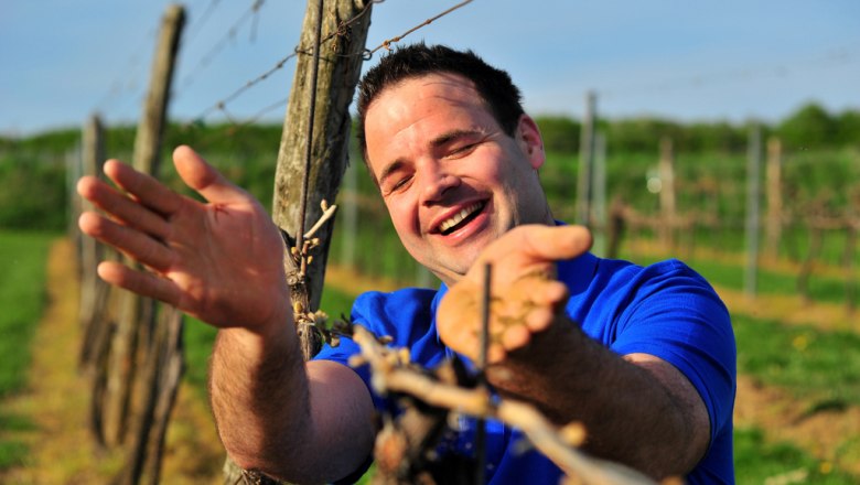 Winzer Andreas Urban, © Seymann Mann in blauem Hemd lächelt in einem Weinberg.