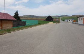 Wohnmobilstellplatz, © Gemeinde Niederleis Ein leerer Parkplatz mit umliegenden Gebäuden und Feldern im Hintergrund.