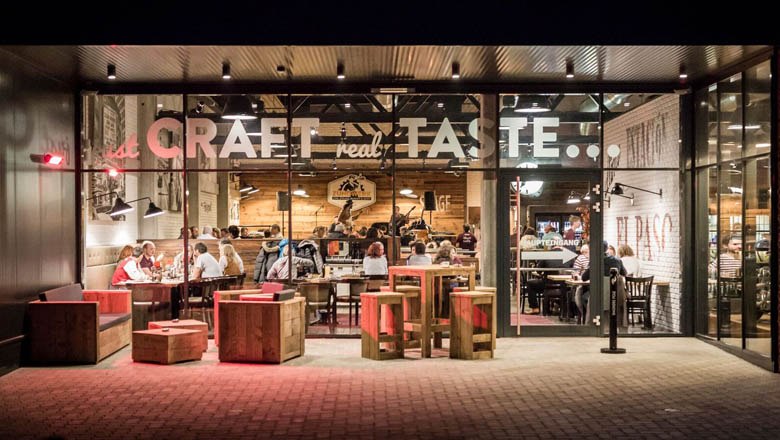 Zündwerk, © Lukas Kirchgasser Photography Außenansicht eines Restaurants mit Glasfront und Holzmöbeln.