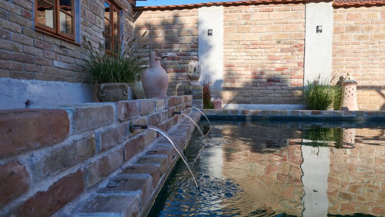 Mediterranean flair in the Weinviertel, © Michaela Wannemacher Brick wall with gargoyles and plants at the edge of a pool.