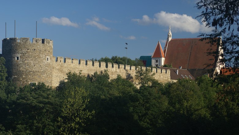 Kanzlerturm mit Stadtmauer und Pfarrkirche, © Veigl Harald Stadtmauer mit Kanzlerturm und Pfarrkirche im Hintergrund, umgeben von Bäumen.