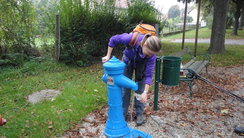 Trinkbrunnen, © Weinviertel Tourismus GmbH Eine Person füllt eine Flasche an einem blauen Trinkbrunnen im Freien auf.