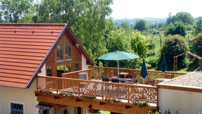 Terrasse, © Familie Arocker Terrasse mit Holzzaun, Sonnenschirm und Gartenmöbeln, umgeben von grüner Landschaft.