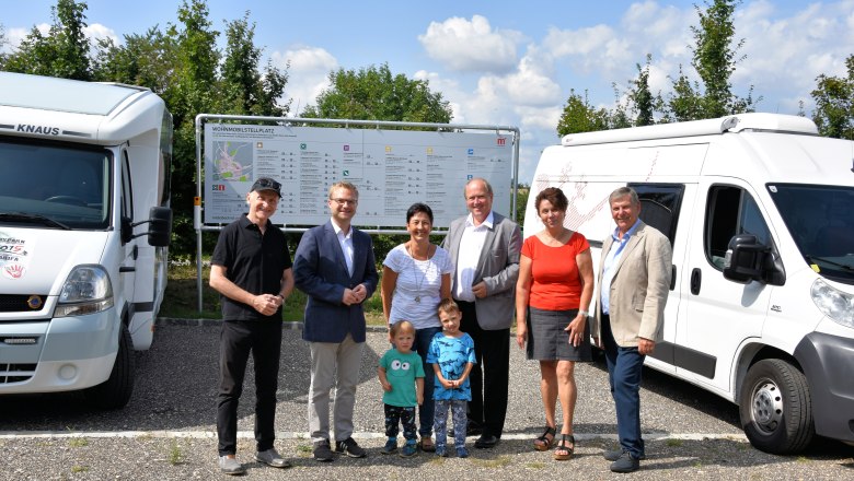 Wohnmobilstellplatz, © Stadtgemeinde Mistelbach Gruppe von Menschen vor Wohnmobilen und einem Schild auf einem Stellplatz.