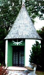 Hubertuskapelle, © Gemeinde Haringsee Kleine Kapelle mit spitzem Dach und Kreuz auf der Spitze, umgeben von Bäumen.