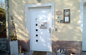 Herzlich Willkommen!, © S. Gritsch-Stockinger Eingangsbereich eines Hauses mit dekorativen Elementen wie einem Hasen, einem Willkommensschild und Blumen.