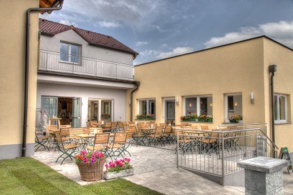 Heurigenlokal, © Fam. Falk Ein gemütlicher Außenbereich mit Holztischen und -stühlen vor einem gelben Gebäude.