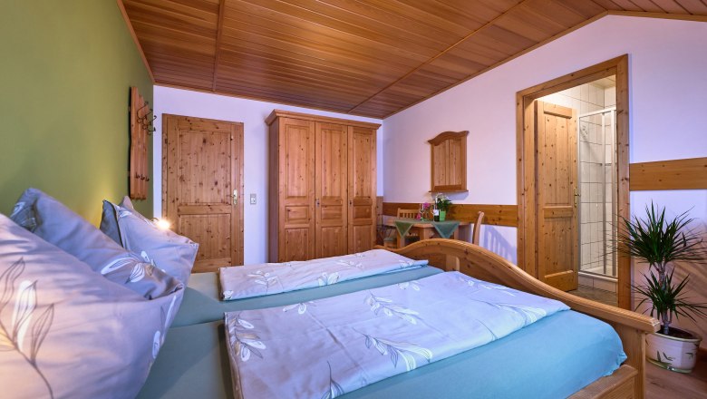 Guest room, © Seher Cozy bedroom with wooden furniture, double bed, closet and small table. A door leads to a bathroom.