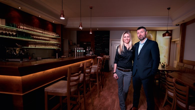 Mährische Botschaft, © tonality Zwei Personen stehen in einer stilvollen Bar mit Holztheke und Gläserregalen.