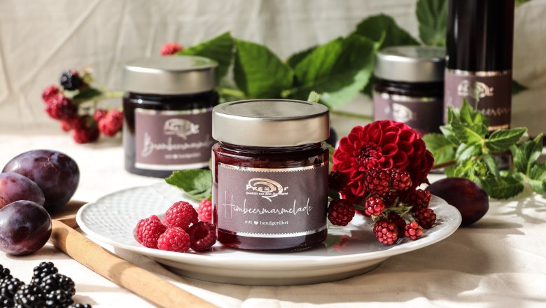 Beerenhof Prenner, © Trixi Rollin Ein Glas Himbeermarmelade auf einem Teller mit frischen Beeren und Blumen dekoriert.