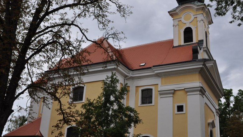 Maria Bründl Poysdorf, © Weinviertel Tourismus Yellow church with red roof and tower, surrounded by trees.
