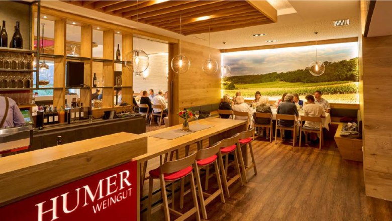 Wine tavern & Humer winery, © Peter Ableidinger Interior view of a modern wine tavern with wooden furniture and a large photo wallpaper of a vineyard.