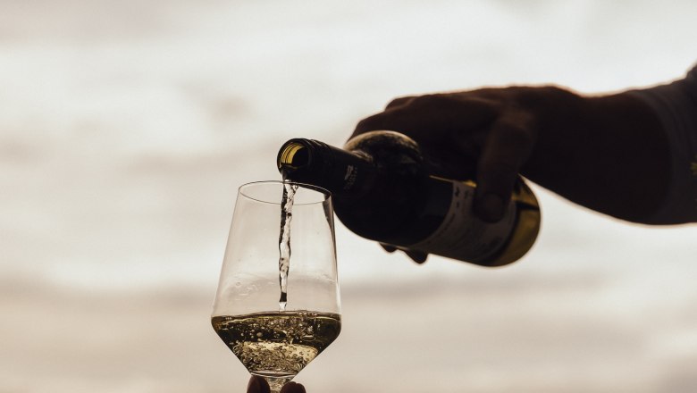 Wein einschenken, © Weinviertel Tourismus / Sophie Menegaldo Wein wird in ein Glas im Freien eingeschenkt, mit einem bewölkten Himmel im Hintergrund.