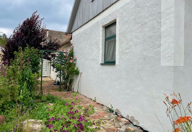 Außenansicht, © Julia Grünschachner Außenansicht eines Hauses mit weißer Wand, Garten und Blumen.