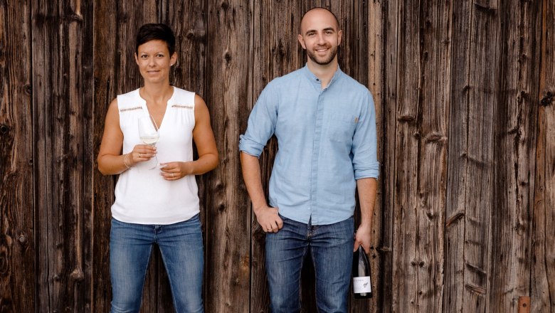 Winery Jatschka, © Astrid Bartl Two people are standing in front of a wooden wall, a woman with a wine glass and a man with a wine bottle.