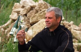 Ein Gläschen in Ehren, © Salomon Mann hält Weinglas vor Steinhaufen im Freien.