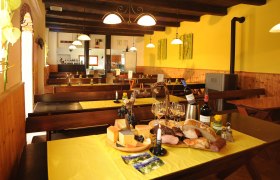 Heuriger Platz-Schwayer, © Schwayer Innenansicht eines gemütlichen Heurigen mit Holztischen, gelben Tischdecken und einer Auswahl an Käse, Brot und Wein auf einem Tisch.