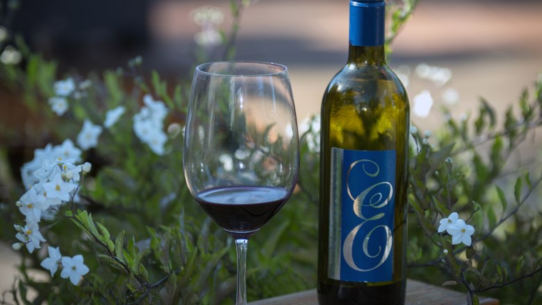 Wein vom Weingut Edenhof, © Leopold Pluschkowitz Weinflasche und Glas auf Holztisch mit Blumen im Hintergrund.