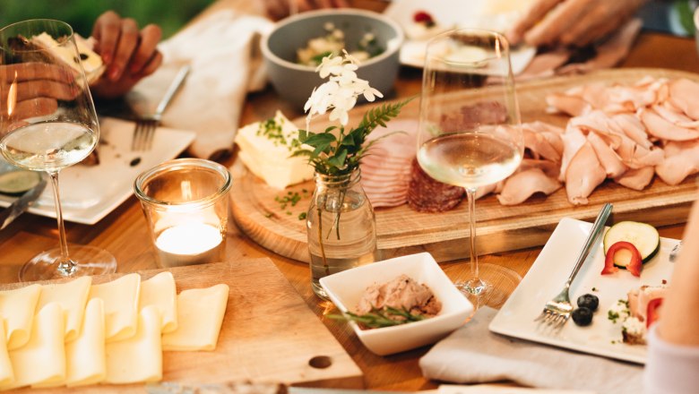 Heurigenjause, © NÖ Werbung / Julius Hirtzberger Ein gedeckter Tisch mit Brot, Käse, Aufschnitt und Weingläsern im Freien.