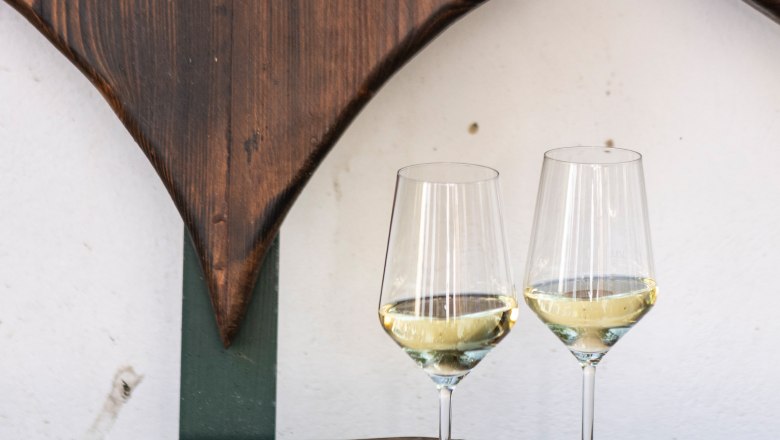 Weingläser, © Weinviertel Tourismus / Doris Schwarz-König Zwei Weingläser mit Weißwein auf einem Holztisch vor einer herzförmigen Holzdekoration.