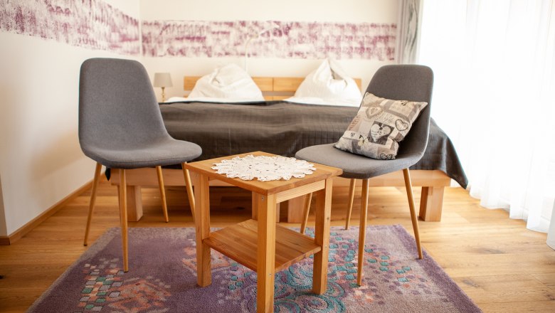 Sitzmoeglichkeit, © Michael Sokolar Zwei graue Stühle und ein Holztisch mit Deckchen in einem Schlafzimmer.
