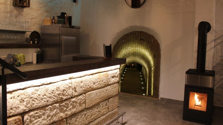 Vinothek, © Weingut Kerner Innenansicht einer Vinothek mit Theke, Kamin und beleuchtetem Tunnel.