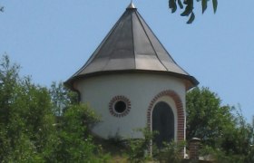 Wasserturm Kammersdorf, © Marktgemeinde Nappersdorf-Kammersdorf Ein runder Wasserturm mit spitzem Dach und Wetterfahne, umgeben von Bäumen und Wiese.