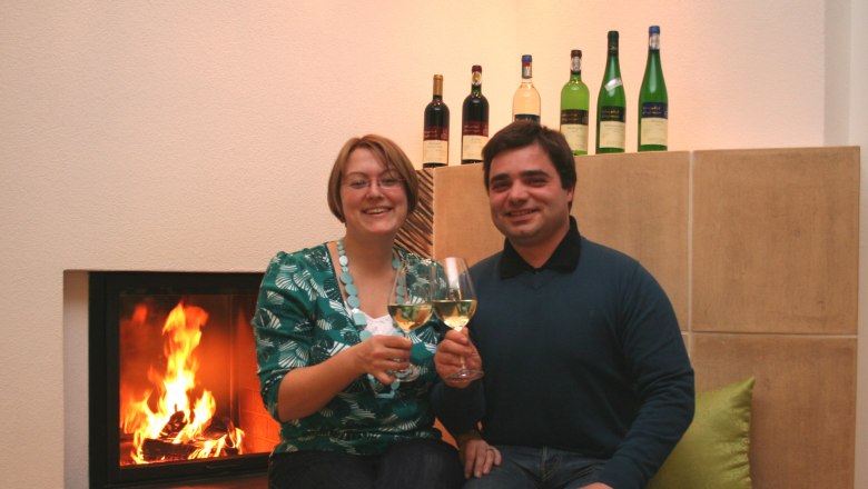 Host, © Kurt Englmayer A couple is sitting in front of a fireplace, clinking glasses of wine.