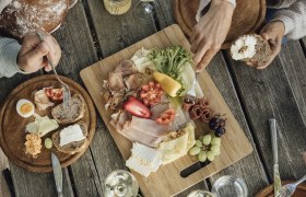 Heurigenjause, © Weinviertel Tourismus GmbH / Sophie Menegaldo Ein rustikaler Holztisch mit einer Jause aus Brot, Käse, Wurst, Gemüse und Wein.