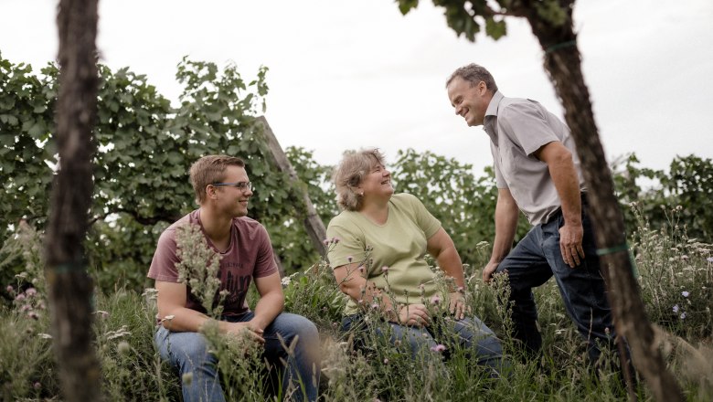 Winzerfamilie Pfalz, © Astrid Bartl Drei Personen in einem Weinberg, die miteinander lachen.