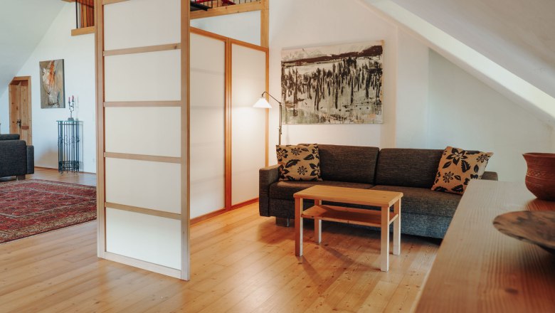 Schlafecke, © Weinakademie Retz Gemütliche Sitzecke mit Sofa, Couchtisch und Raumteiler in einem Dachgeschosszimmer.