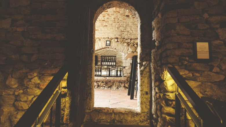 Wine shop, © Michael Reidinger Stone wall with passageway to a room with bottles on a shelf.