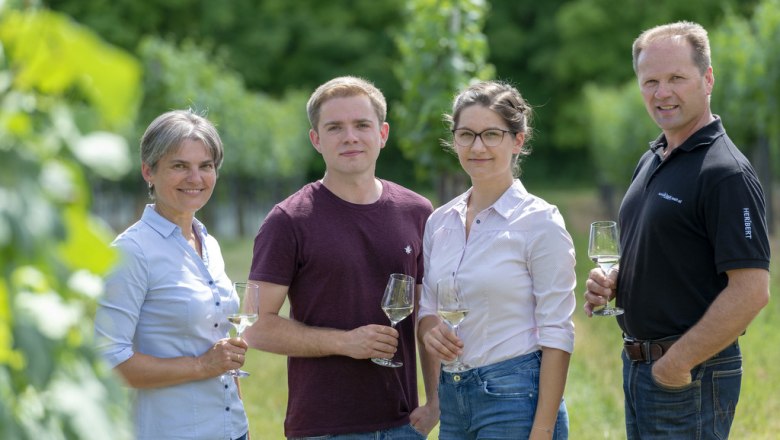 Familie Wenzl, © Michael Himml Vier Personen stehen in einem Weinberg und halten Weingläser.