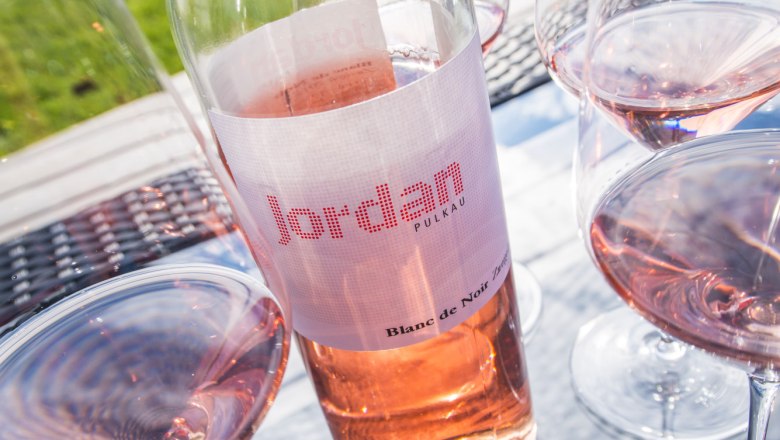 Jordan Wein, © Petr Blaha Weinflasche und Gläser mit Roséwein auf einem Tisch im Freien.