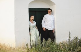 Wirtsleute Daniela und Harald Graf, © Niederösterreich Werbung/Michael Reidinger Zwei Personen stehen in einem Türrahmen vor einem weißen Gebäude.