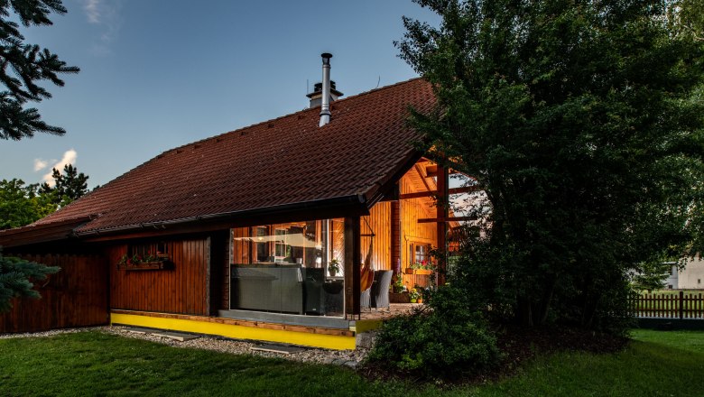 Außenansicht, © Imre Antal Außenansicht eines Holzhauses mit großen Fenstern und Garten, umgeben von Bäumen.