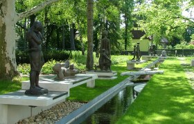 Prof. Knesl Museum, © Marktgemeinde Bad Pirawarth Skulpturengarten mit mehreren Bronzefiguren und einem Wasserlauf.