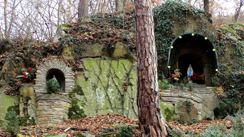 Eye grotto in Straning, © Archiv Grafenberg A stone grotto with a statue of the Virgin Mary and plants, surrounded by trees and foliage.