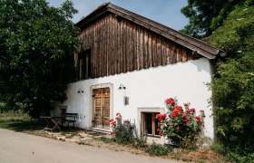 Außenansicht, © Weinakademie Retz Außenansicht eines Hauses mit Holzwänden, weißen Wänden und roten Blumen im Vordergrund.