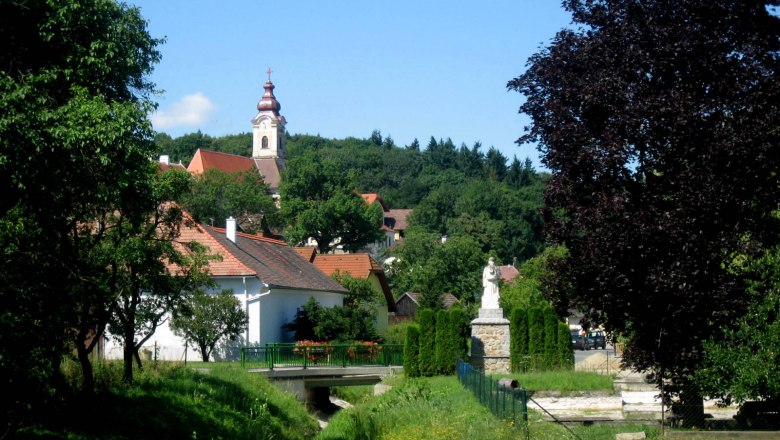 Pfarrkirche Zemling, © Marktgemeinde Hohenwarth-Mühlbach Landschaft mit Kirche und Statue in einem Dorf.