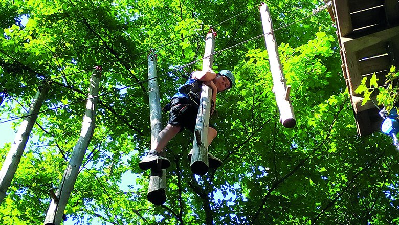 Kletterspaß im Ochys Waldfreizeitpark, © Ochys Waldfreizeitpark Kind klettert im Hochseilgarten zwischen Bäumen.