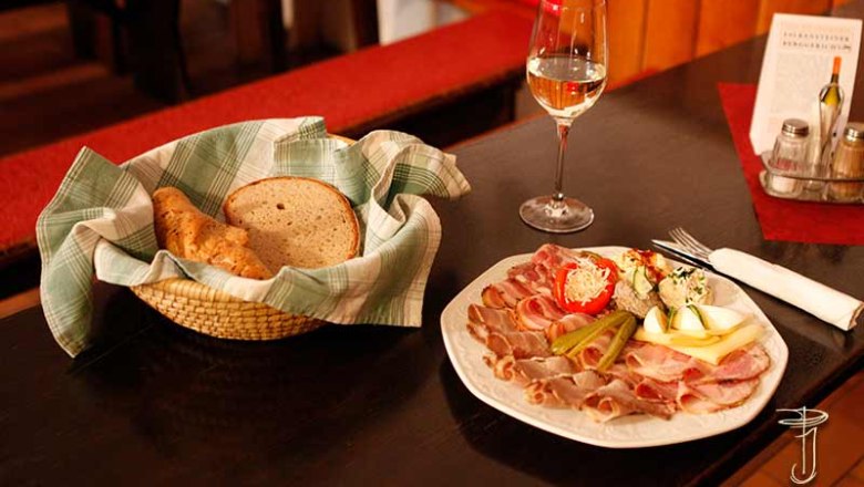 Gmoakeller plate, © Weingut P. Jauk A table laid with a platter of cold meats, a basket of bread and a glass of white wine.