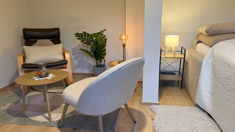 Bedroom, © Waltraud Forstner Cozy bedroom with armchair, table, plant and bed.