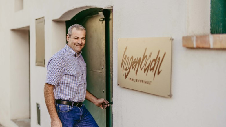 Winemaker, © Christina Wenzina A man opens a door next to a sign that reads 'Hagenbüchl Familienweingut'.